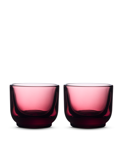 Two Pirch Espresso Glasses by Fellow in transparent dark pink sit side by side on a light background.